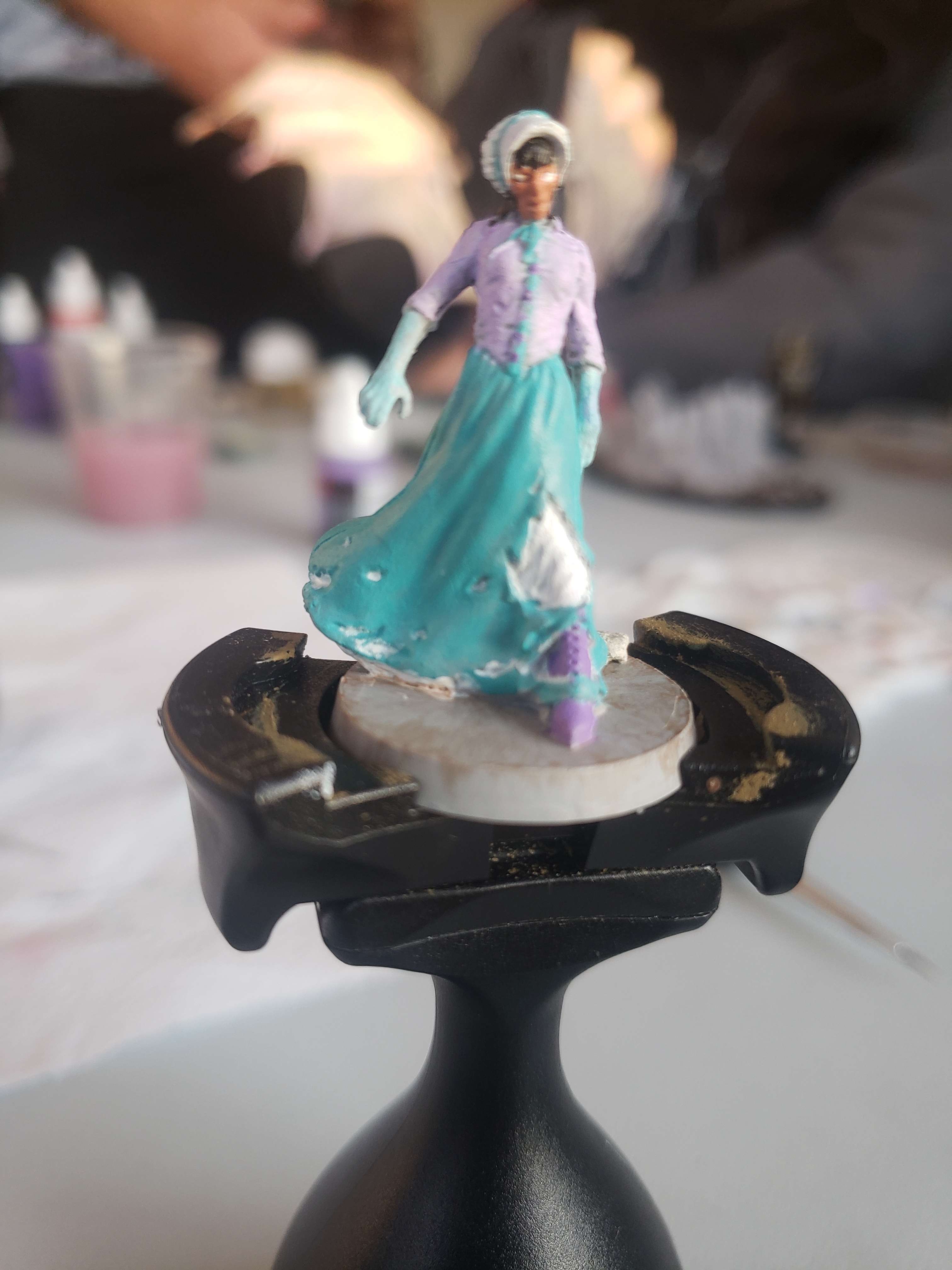 Miniatura de Zombiecide. Una mujer zombie mayor con un vestido lila y turquesa roto y gorrito blanco.
