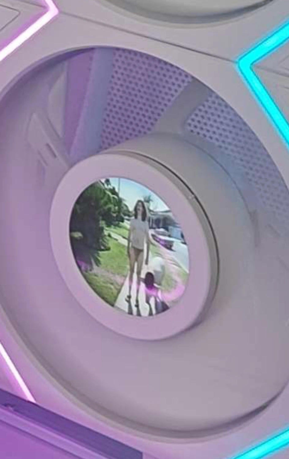 zoomed in screenshot of previous image focused on one of the fan screens showing what appears to be an ambiguously gendered person wearing a thong and walking some large animal (possibly human) on a sidewalk