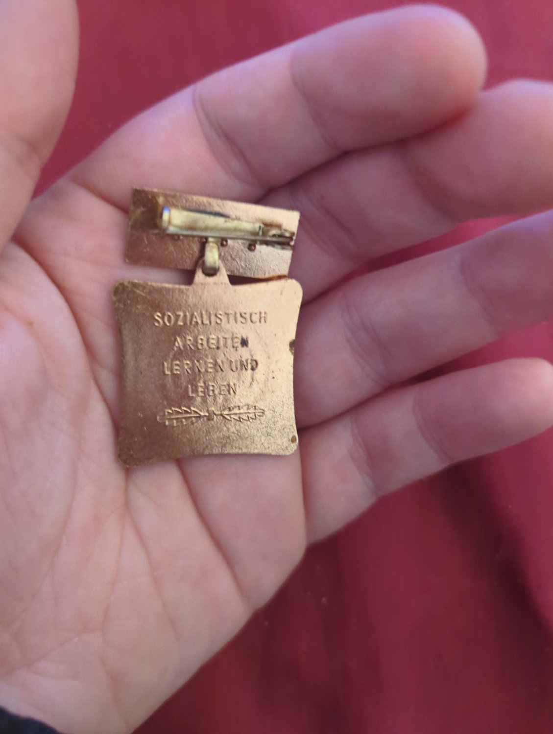 the back of an original GDR pin saying "sozialistisch arbeiteten lernen und leben"