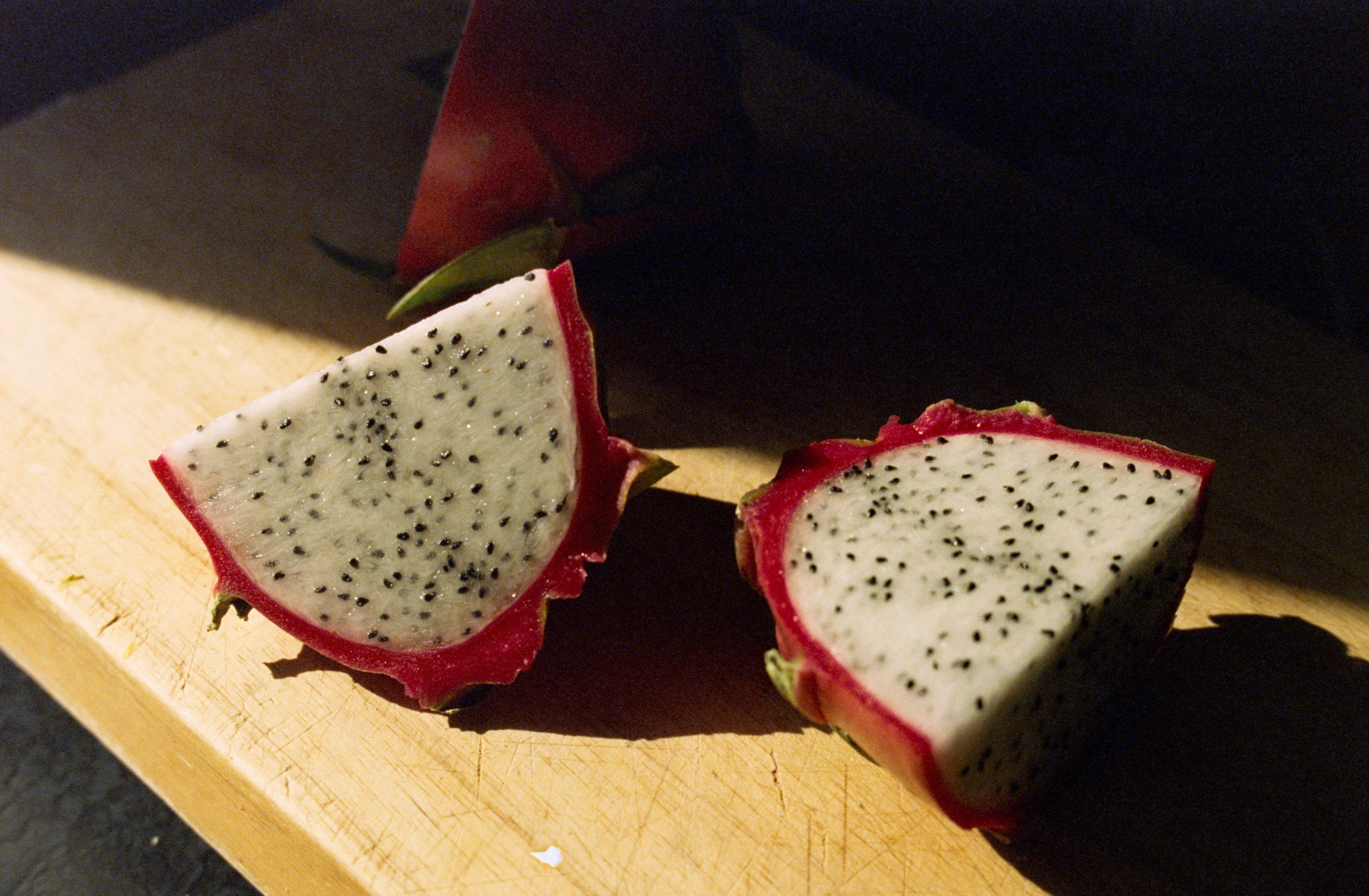 a cut dragonfruit on a wood cutting board lit with a band of sunlight