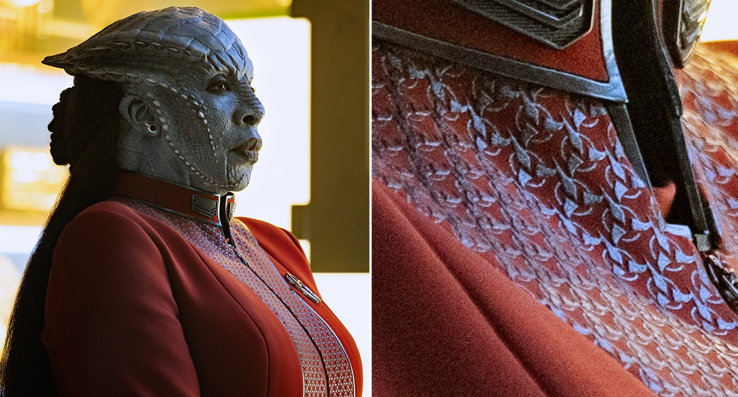 Gina Yashere in grey alien makeup, with horns protruding along her face. She is wearing a red Starfleet uniform with unique patterning. A close-up of the patterning reveals the Klingon Empire symbol.